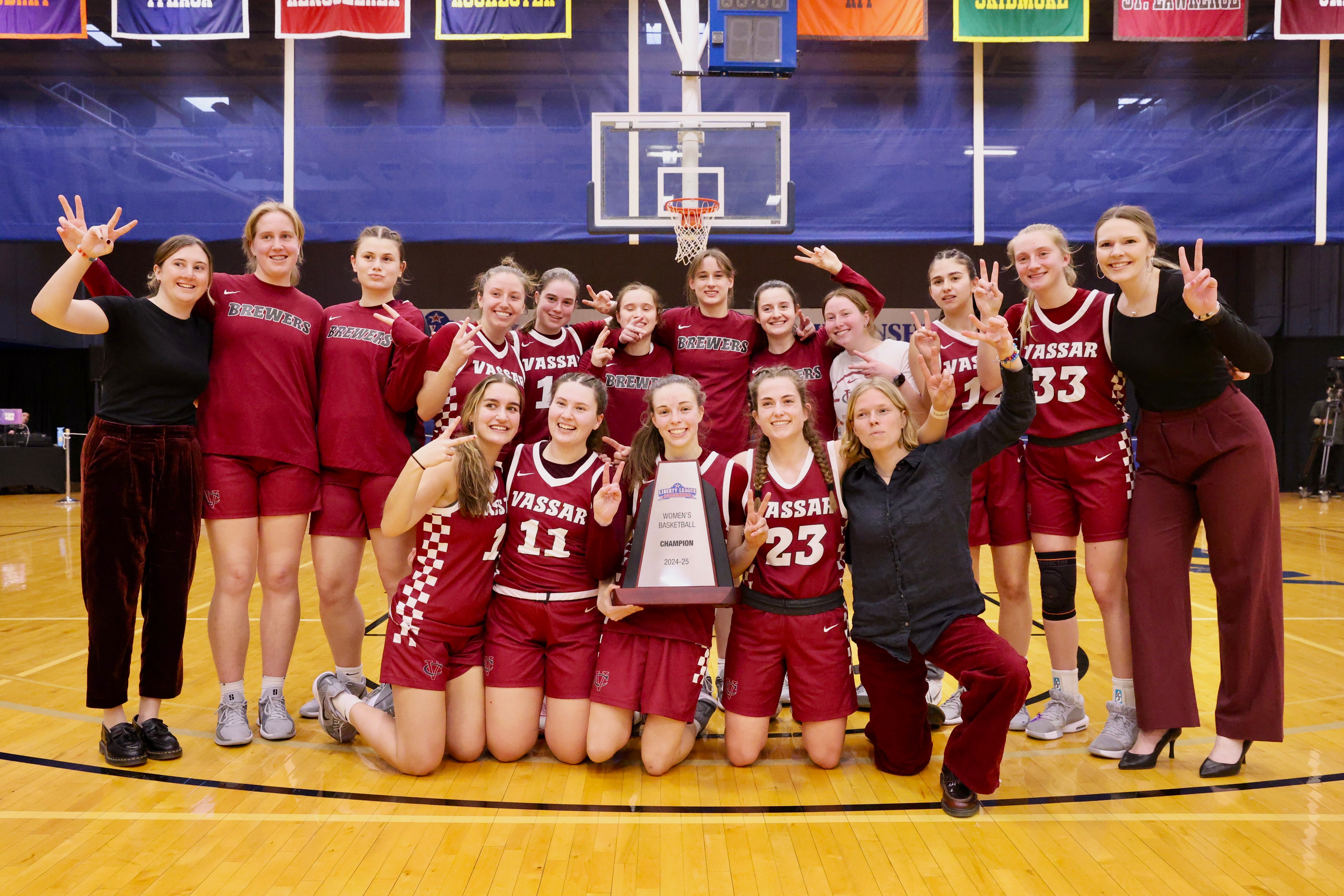 Basketball team and coaches making victory signs with their hand and posing on the court with a trophy.