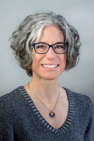 Susan G. Blickstein wearing a gray sweater and silver necklace against a gray background.