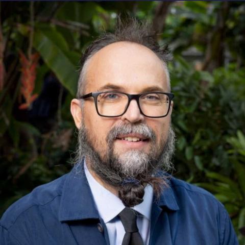 Photo portrait of a person standing in front of green foliage.