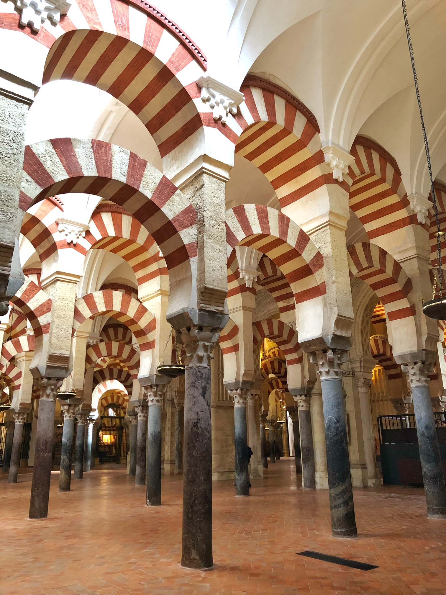 Interior of the Great Mosque of Córdoba, a large room with many columns in rows connected by double arches in light and dark stone.