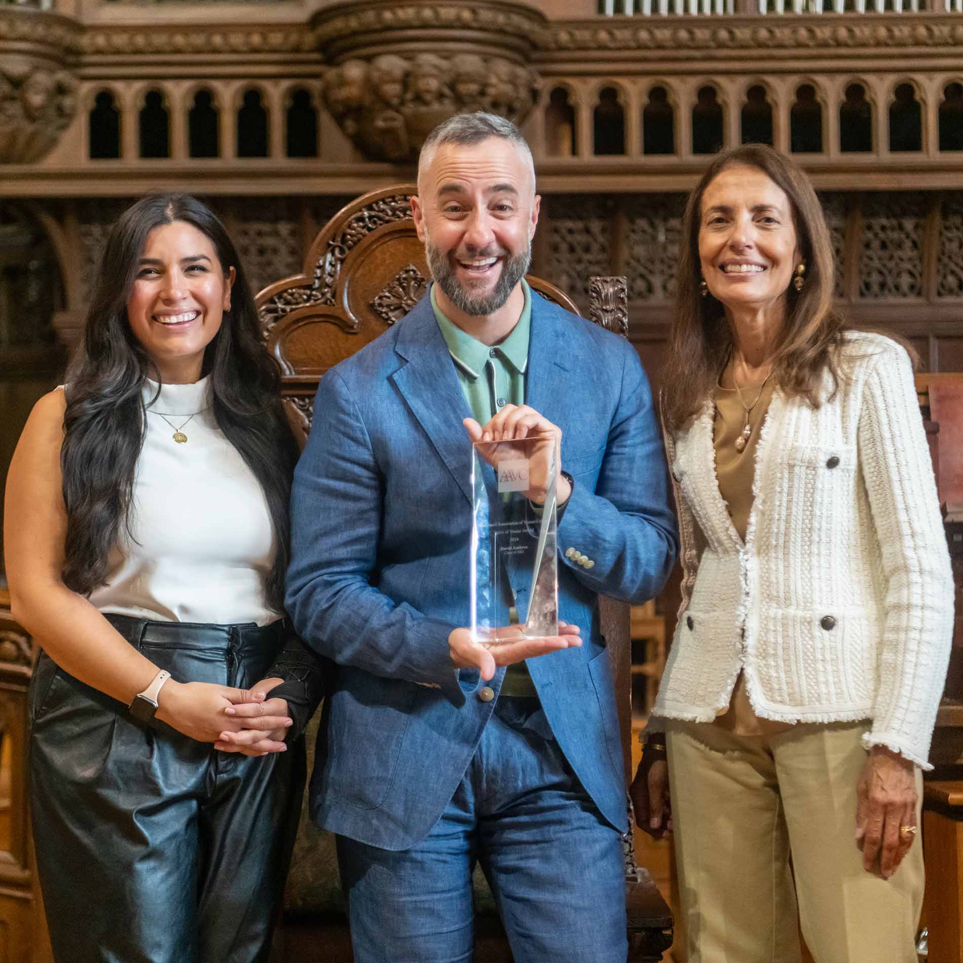 Three people, one of whom is holding a glass award, stand together smiling.