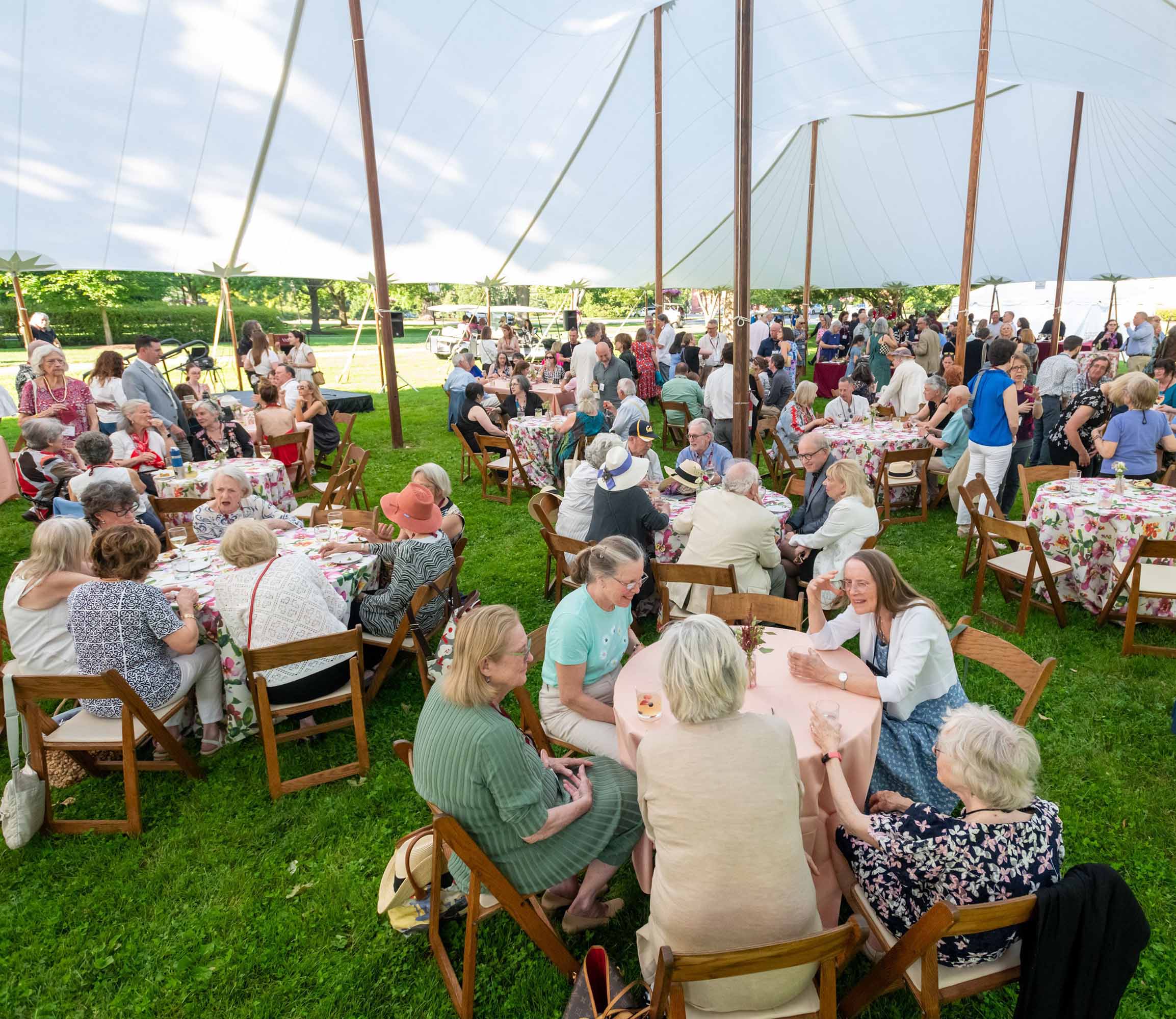 A large group of people sit at tables under a tent.