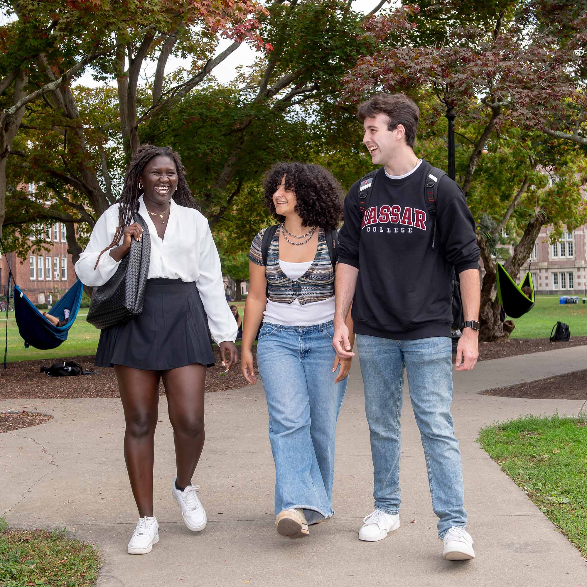 Three students in casual clothing laugh and talk together while walking across the center of Vassar’s quad.