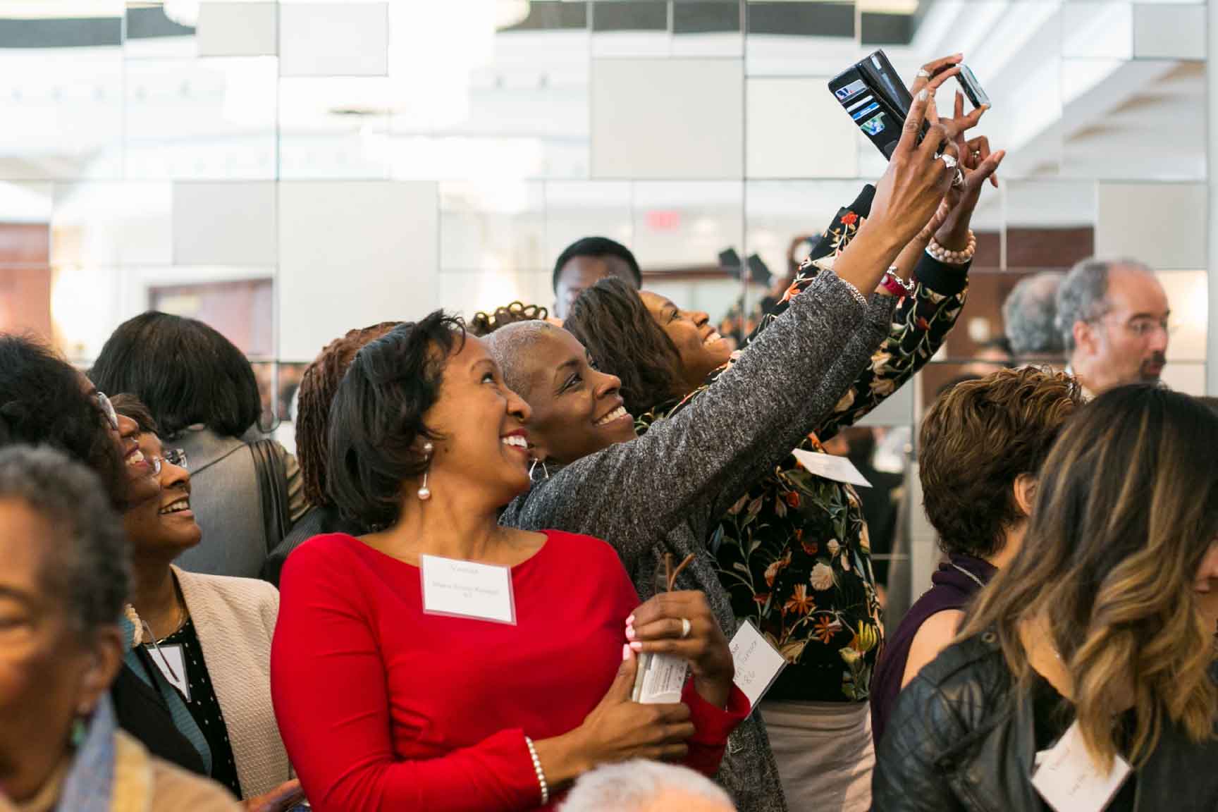 Group of people stand next to each other smiling, taking a selfie at a crowded event.