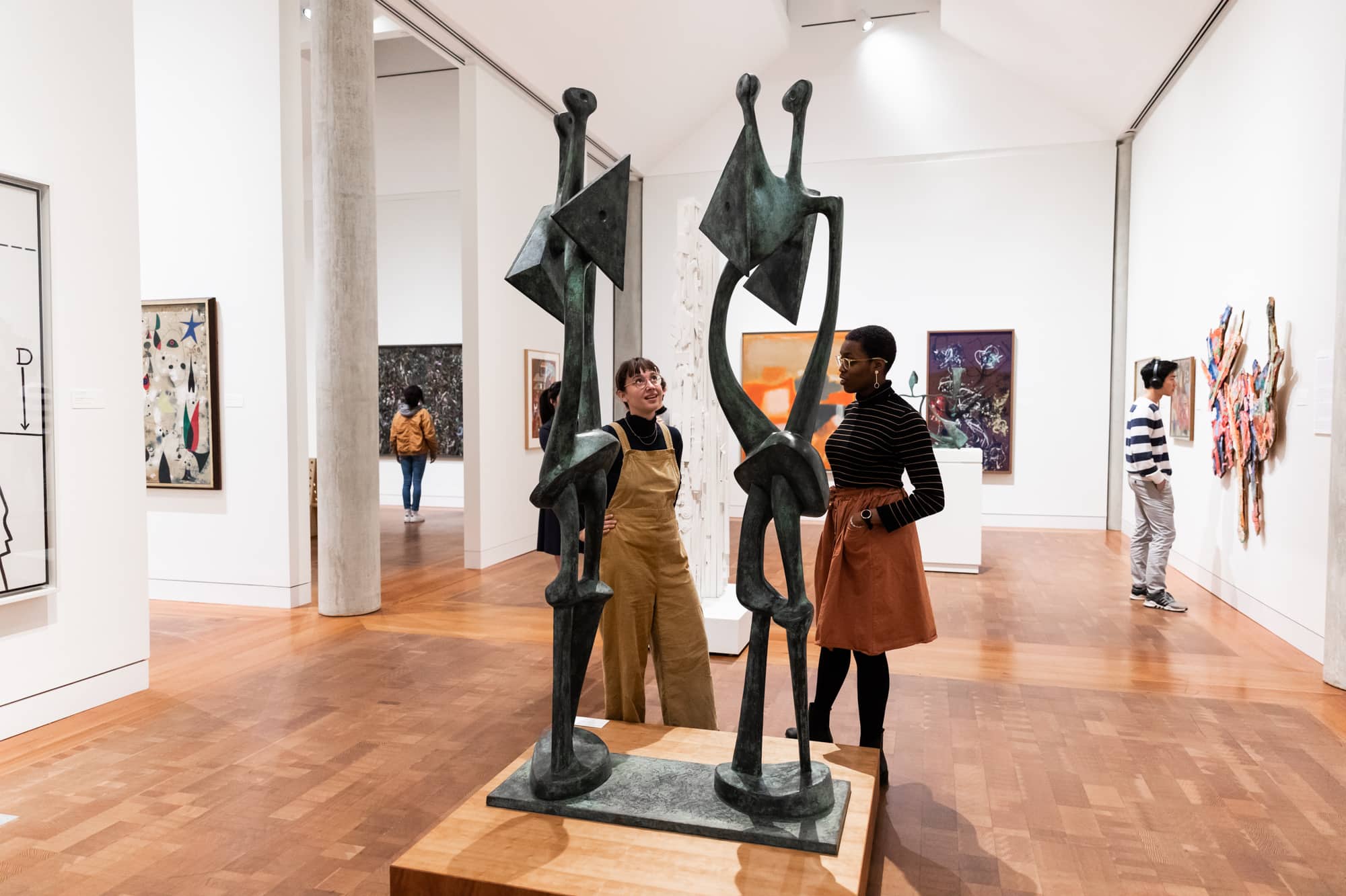 People in an art gallery are looking at a black statue and conversing with one another.