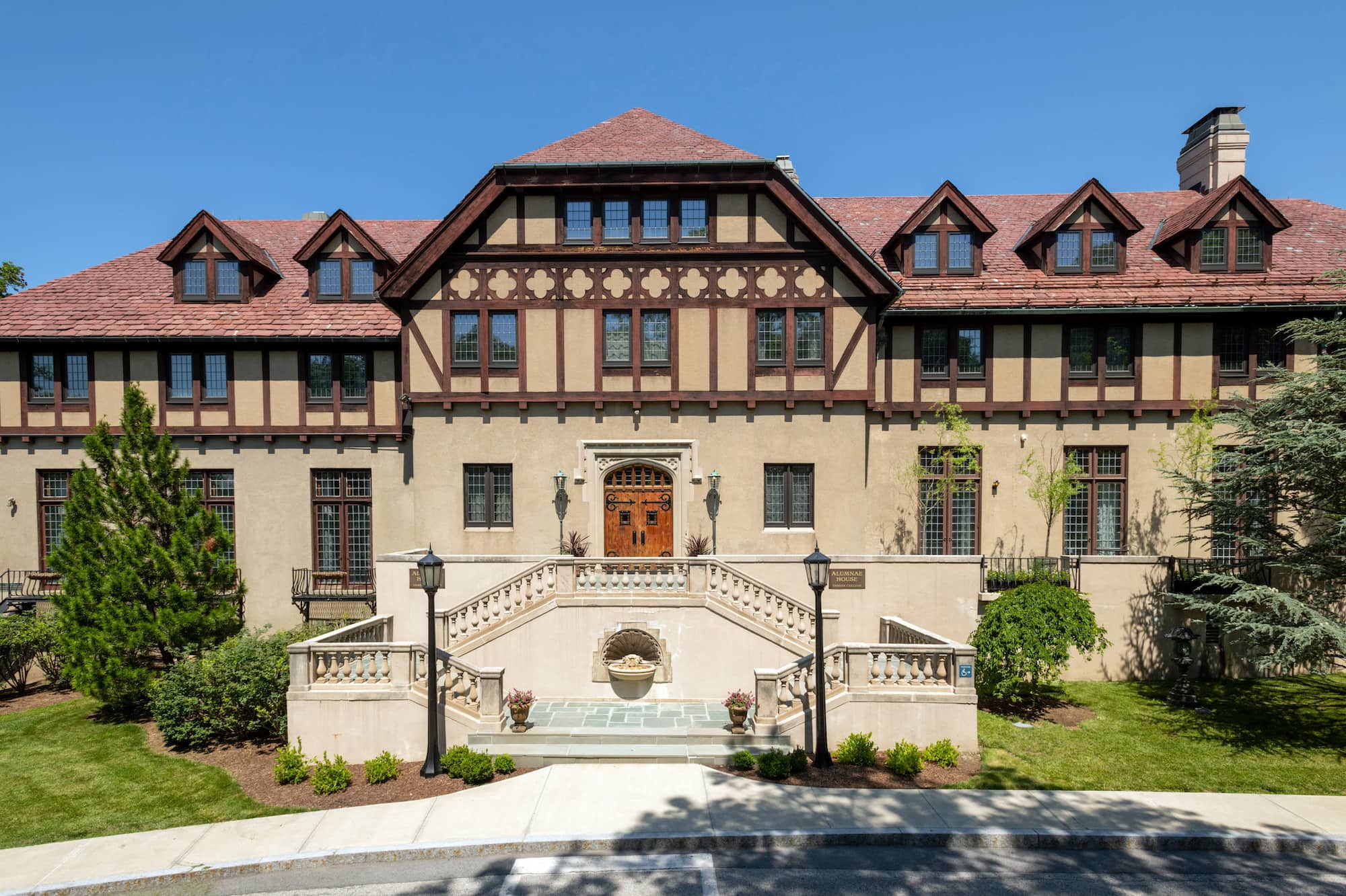 The front exterior of Alumnae House on the Vassar campus, a large beige building with a red roof and many windows across the entire building.