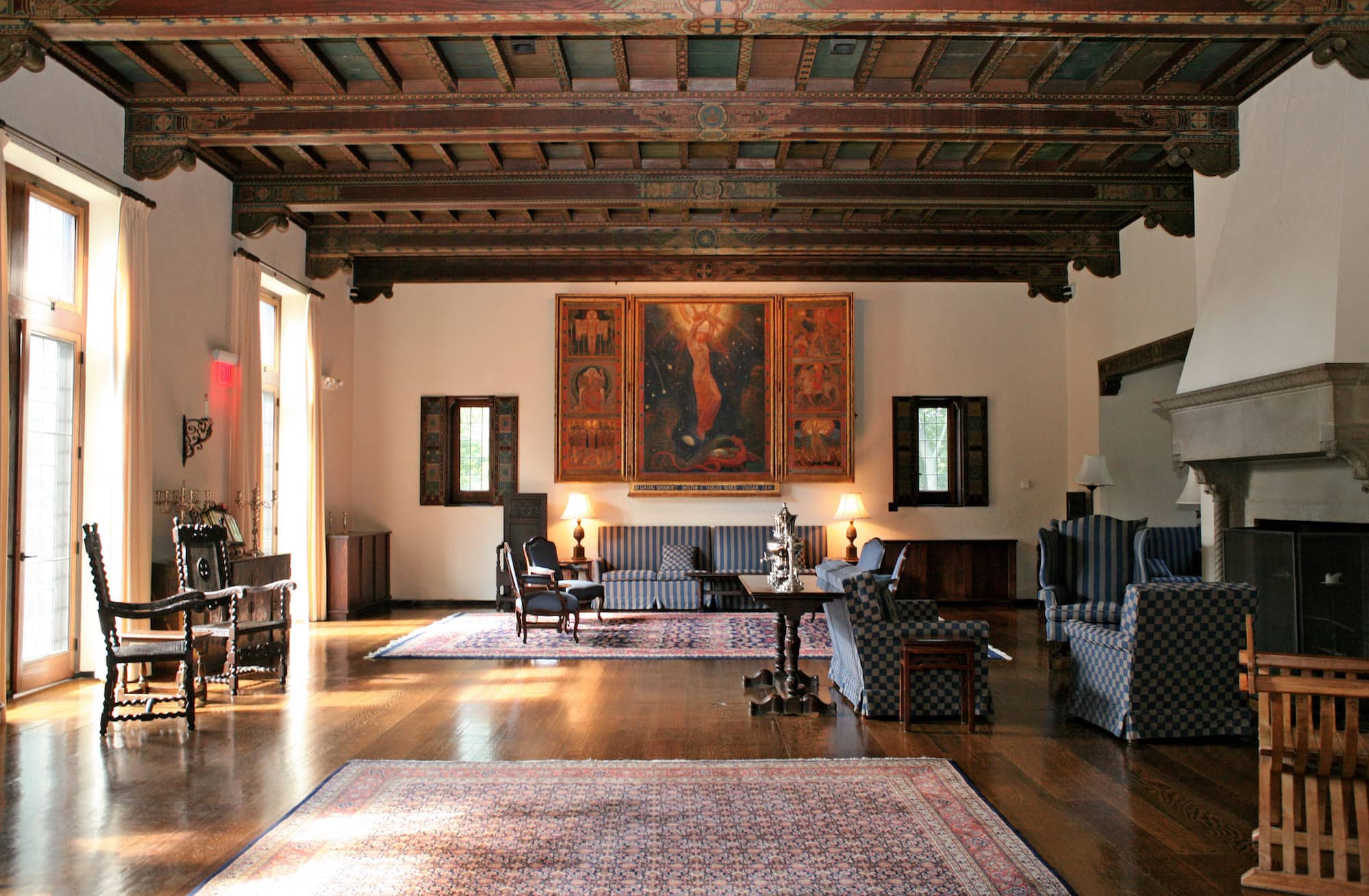 A common area inside Alumnae House on the Vassar campus, a wide space with a patterned wooden ceiling, various seating spaces, and a large painting hanging on the far wall of the room.