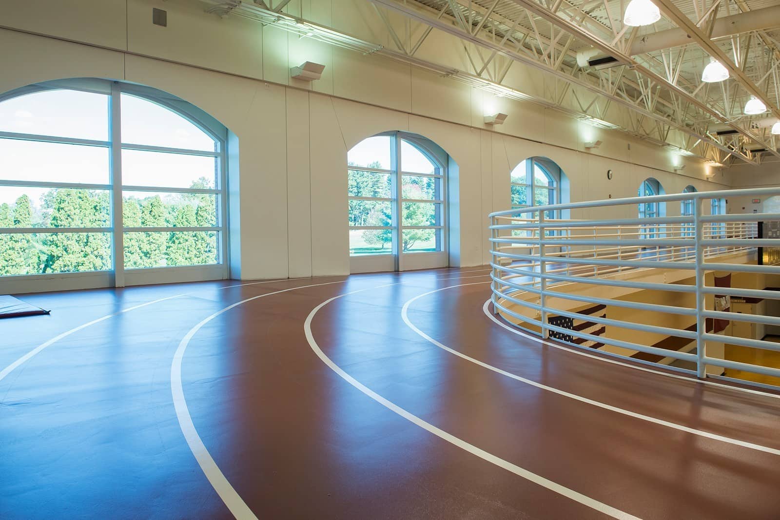 A running track inside the Athletics and Fitness Center at Vassar College, a long brown lane divided into multiple sections with large windows all the way around.
