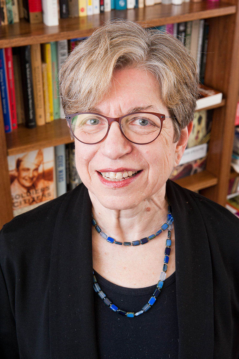 A headshot of Miriam Cohen, a person with short gray hair, glasses, and black clothing.