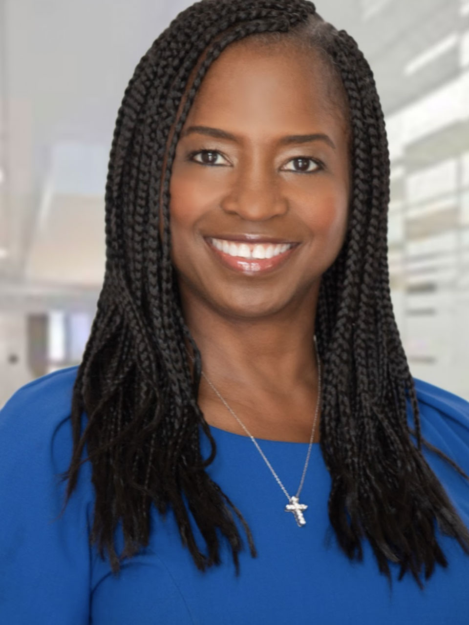 A person with long, black hair in many braids and a blue shirt smiles at the viewer.