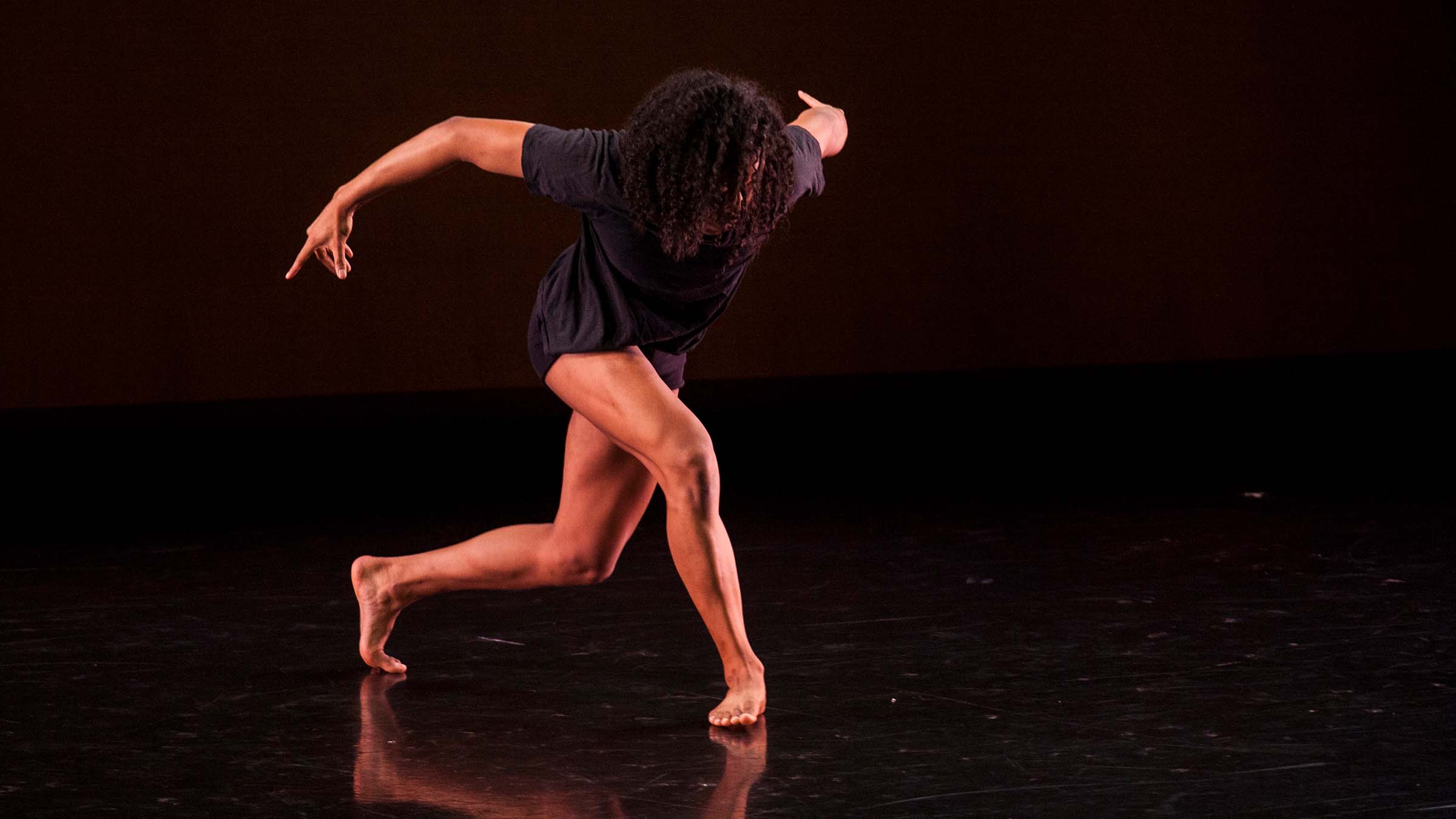 A dancer on a darkened stage crouches in mid-pose. Photo by Rachel Garbade ’15.