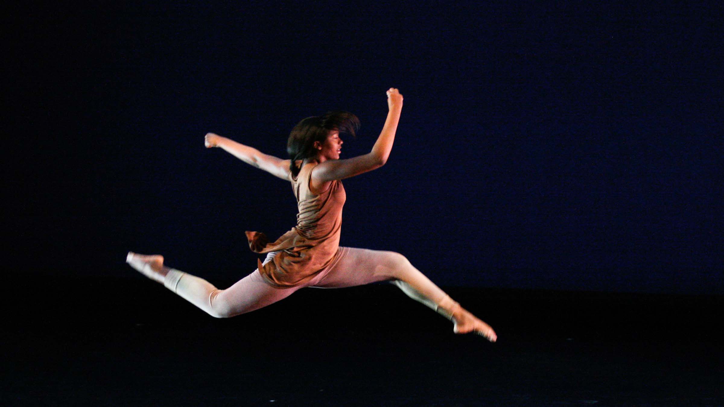 A dancer caught in mid-leap on a darkened stage. Photo by Madeline Zappala ’12.