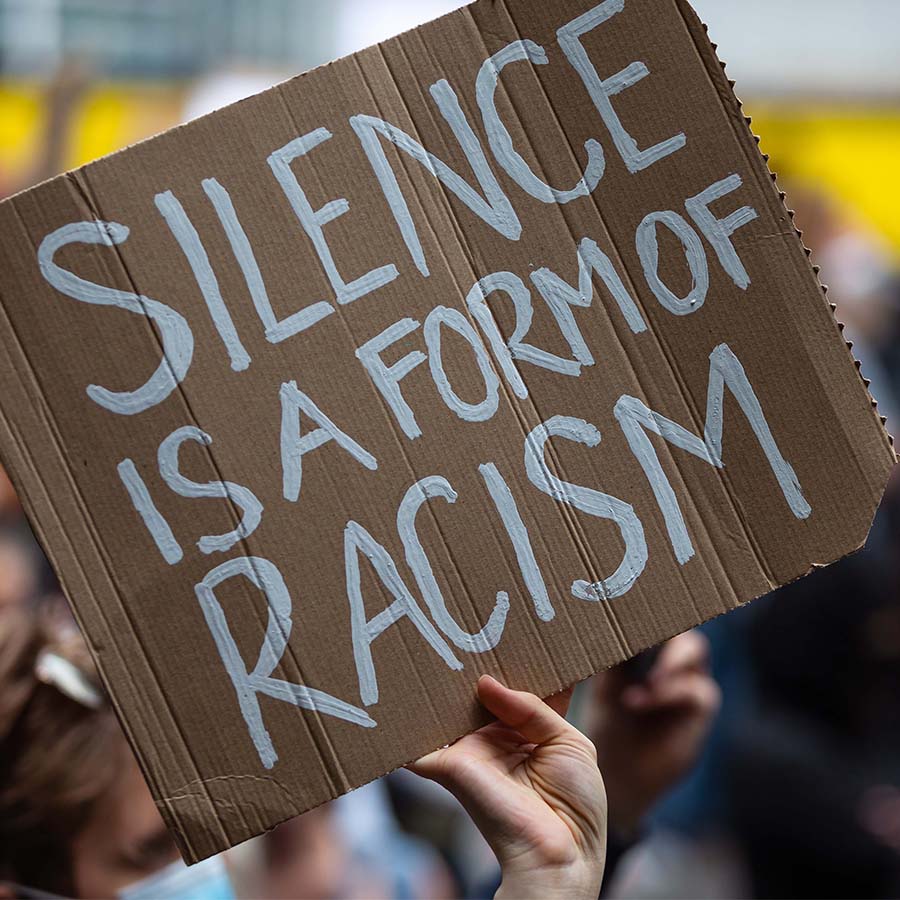 A hand holding up a sign that says, "silence is a form of racism."