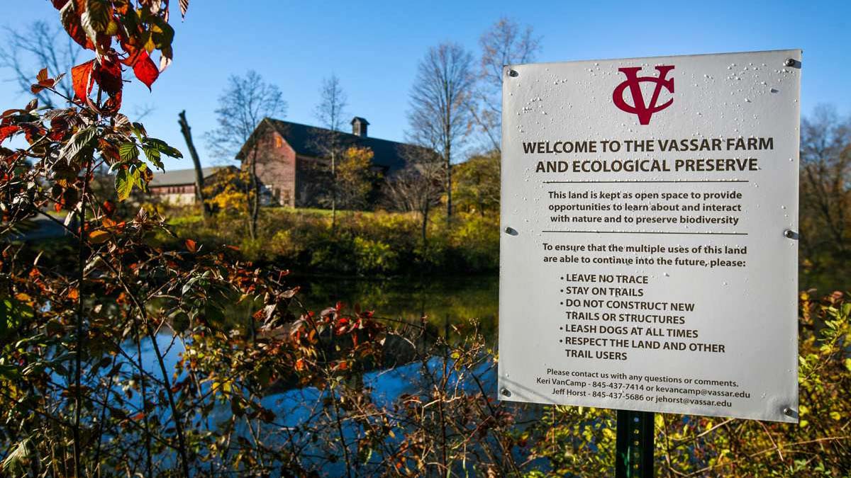 A photo of the Vassar Farm and Ecological Preserve: A pond, with a barn in the distance and a sign in the foreground that reads "Welcome to the Vassar Farm and Ecological Preserve".