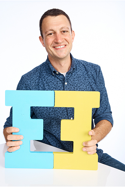 David Flink holding a 3D shape made of two letter E's facing each other, which is the symbol of his organization "Eye to Eye"
