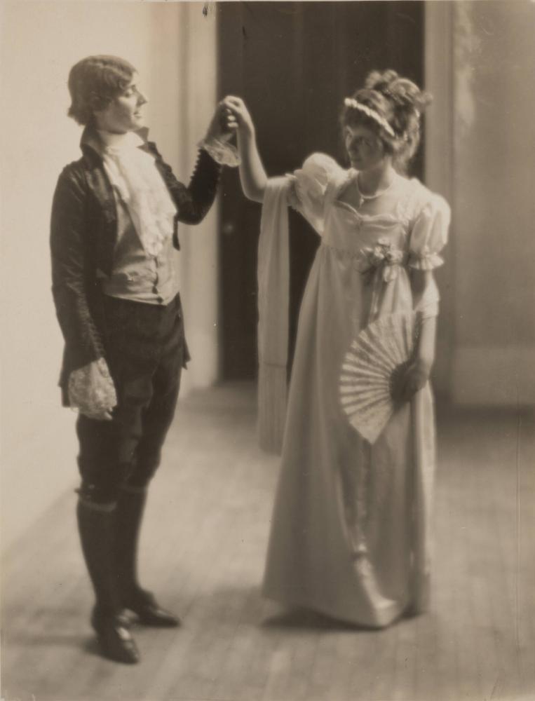 Black and white old photo of a man and woman standing holding hands wearing Victorian style clothing