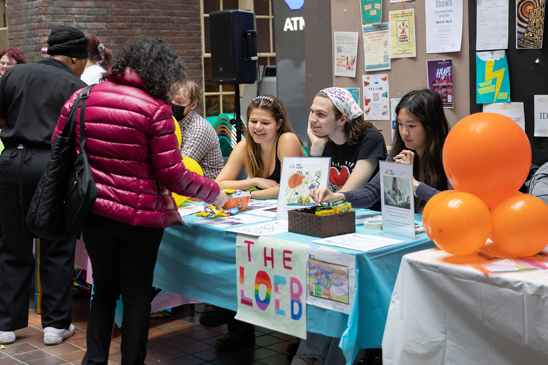 Students sitting at a booth with people standing and talking to them