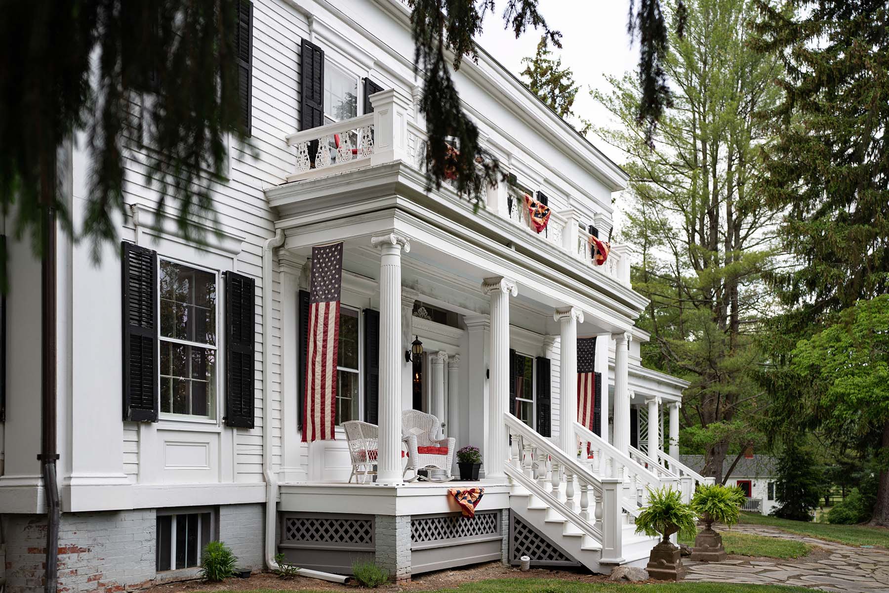 White house with black shutters and a small covered porch with Roman columns