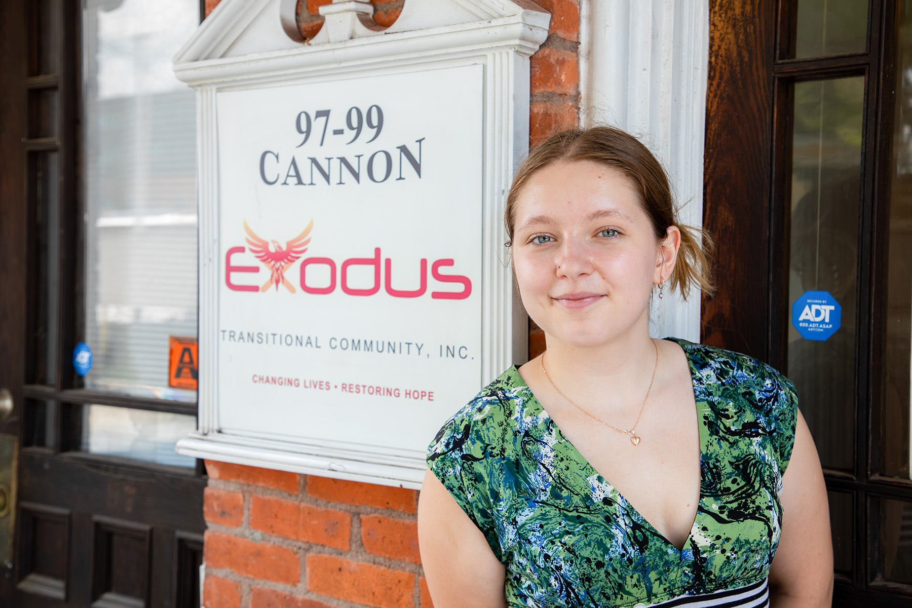 Woman standing in front of a door with a sign that reads, "Exodus: Transitional Community, Inc."