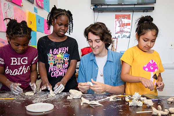 Community Fellow Simon Lewis and three young students work with clay at a long table.