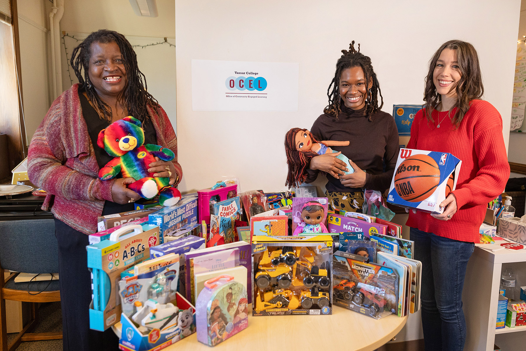 Three people standing in front a table filled with different boxes and presents.