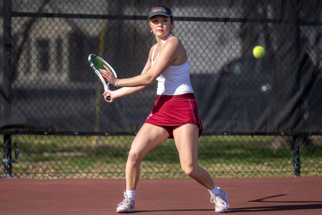 A person wearing red shorts and a white tank top prepares to hit a tennis ball.