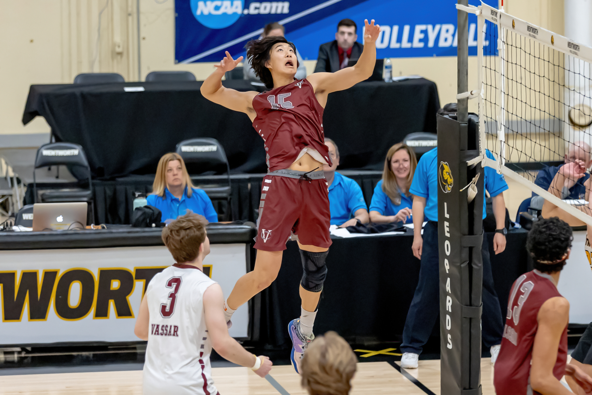 A person with a burgundy tank top and burgundy shorts jumps up to hit a volleyball.