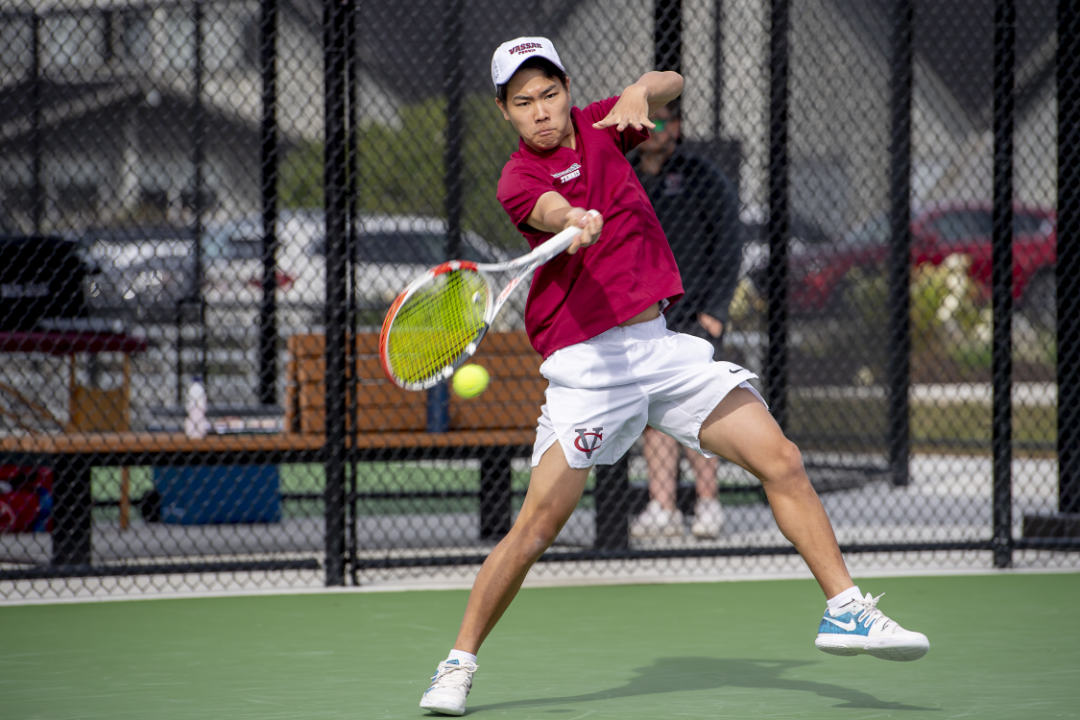 A person wearing white shorts and a red shirt prepares to hit a tennis ball.