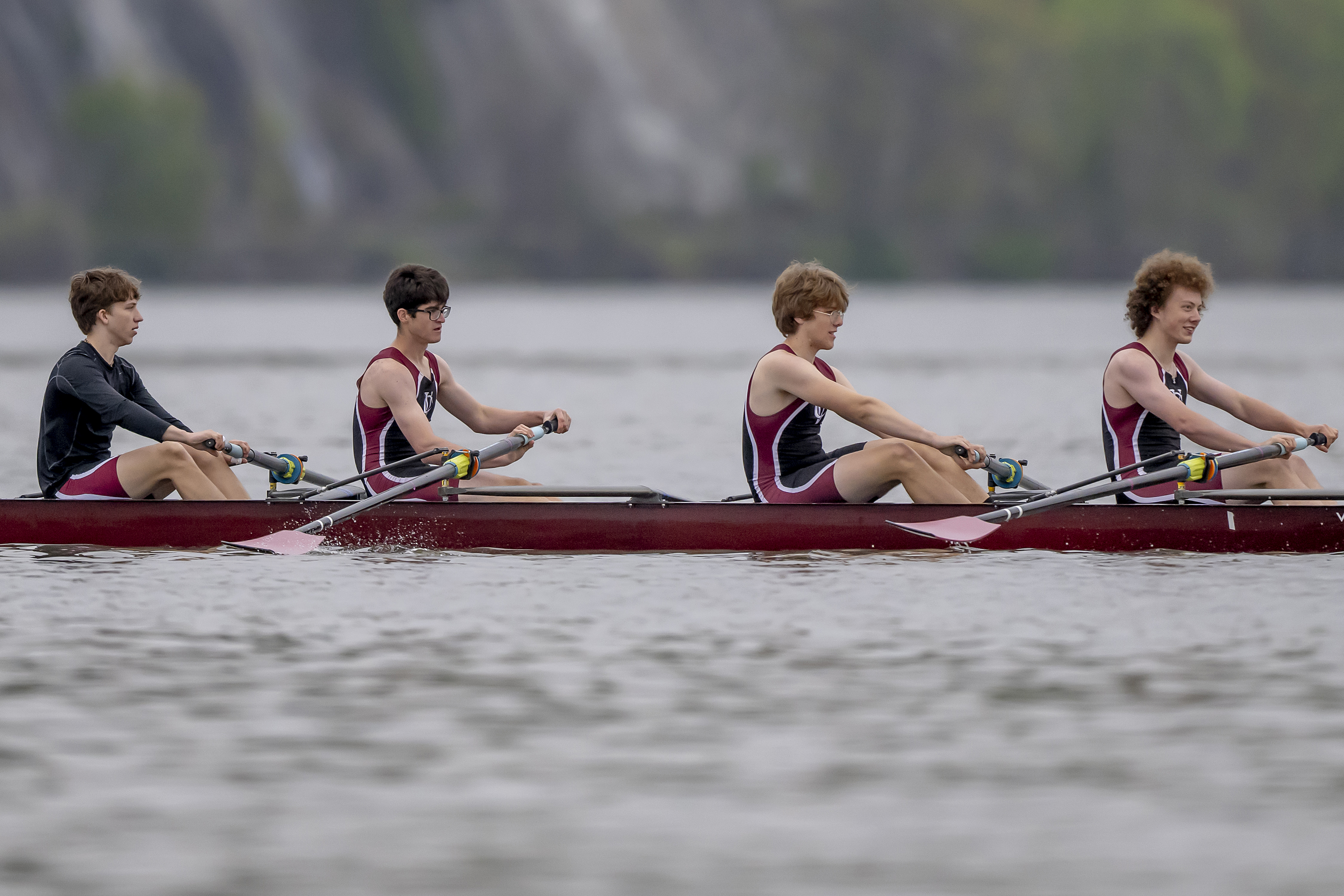 Four men row a boat on the water.