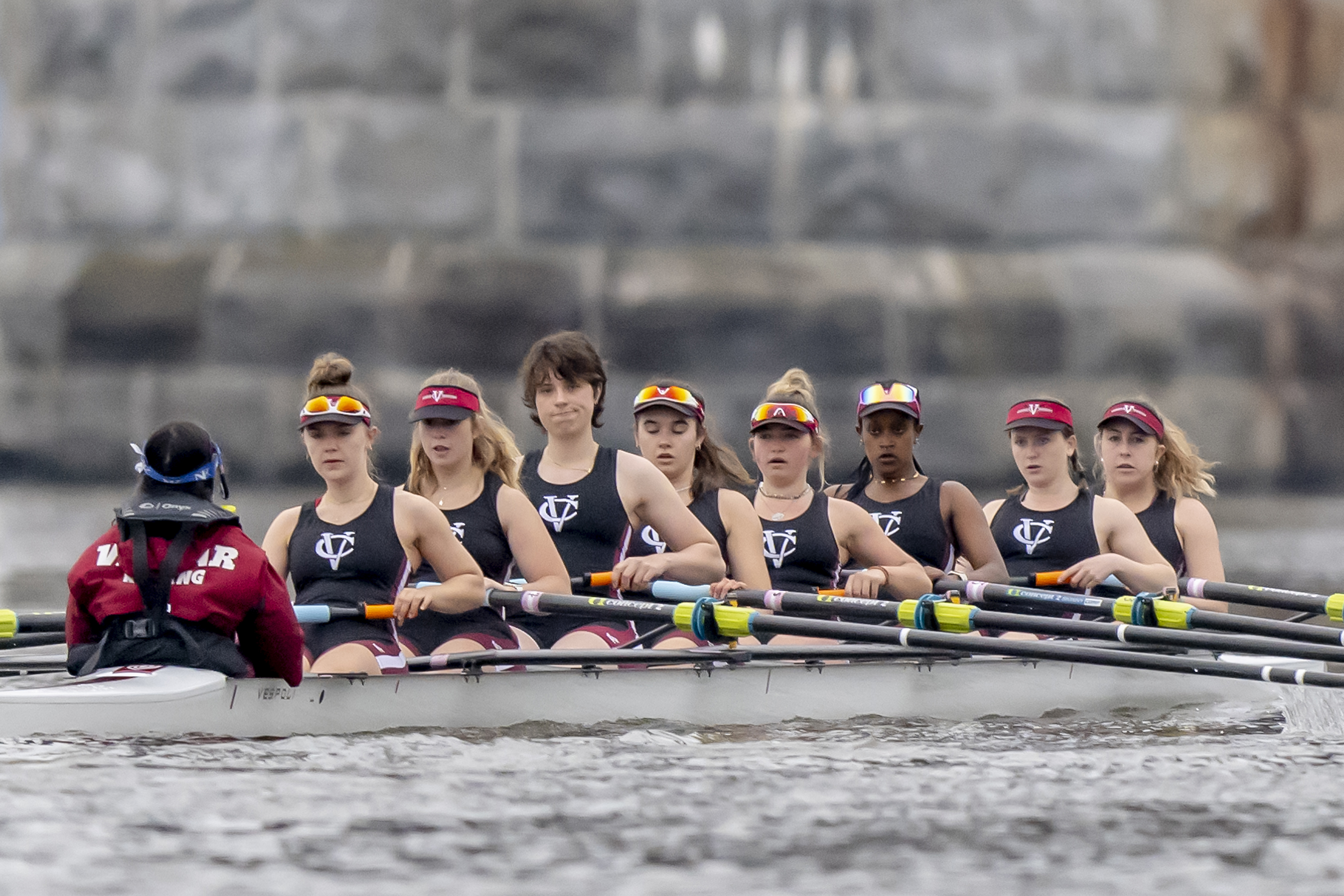 The eight-member women's rowing team, all wearing tank tops with the letters "VC" on them, sit in their boat on the water.