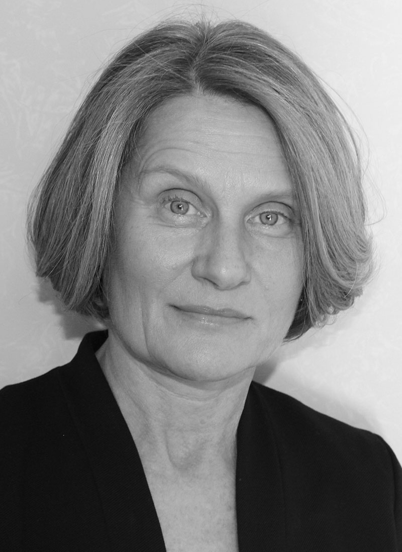 A monochrome headshot of Susan Hiner, a person with short light-colored hair and a dark jacket.