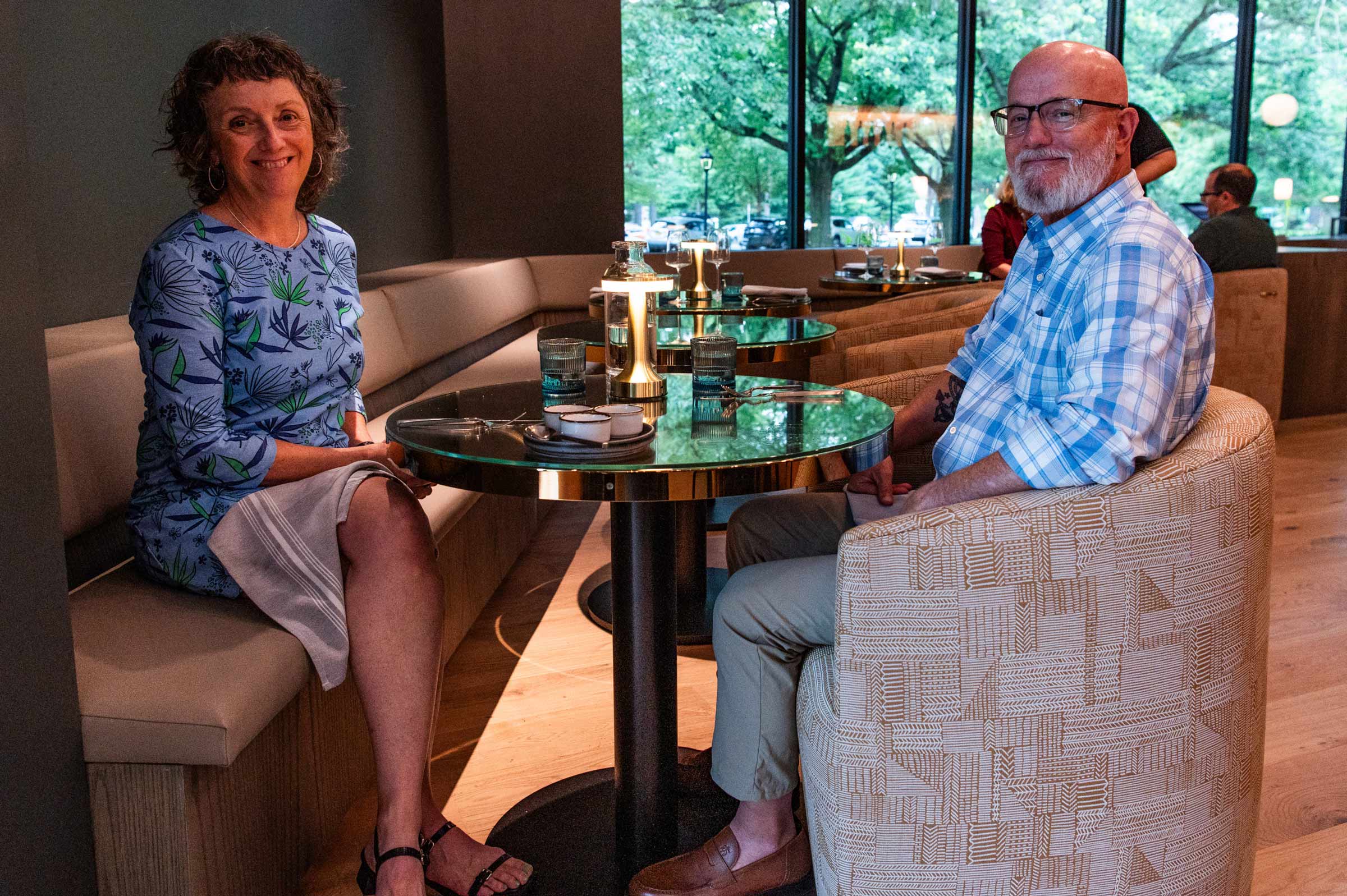 A couple sitting across from each other over a dining table smiling at the camera.