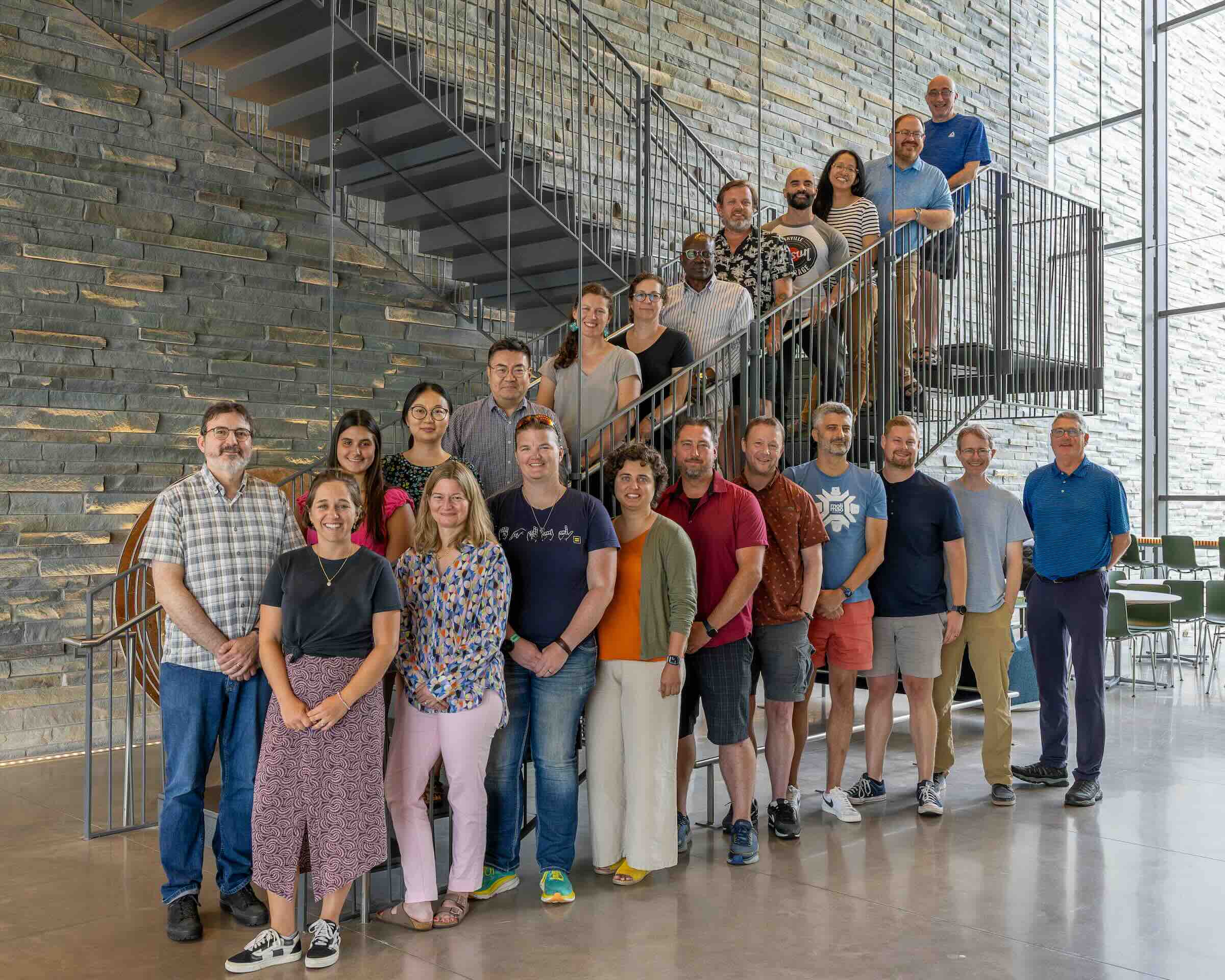 A large group of people arranged on the floor and one flight of a staircase smiling.