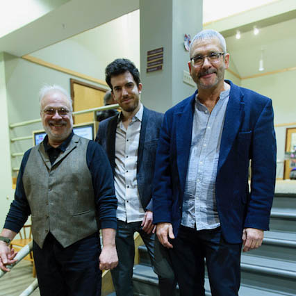 Three people standing on stairs in a building smiling for the camera.