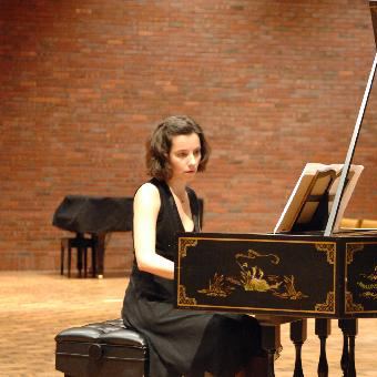 Person sitting and playing at a piano on a stage.