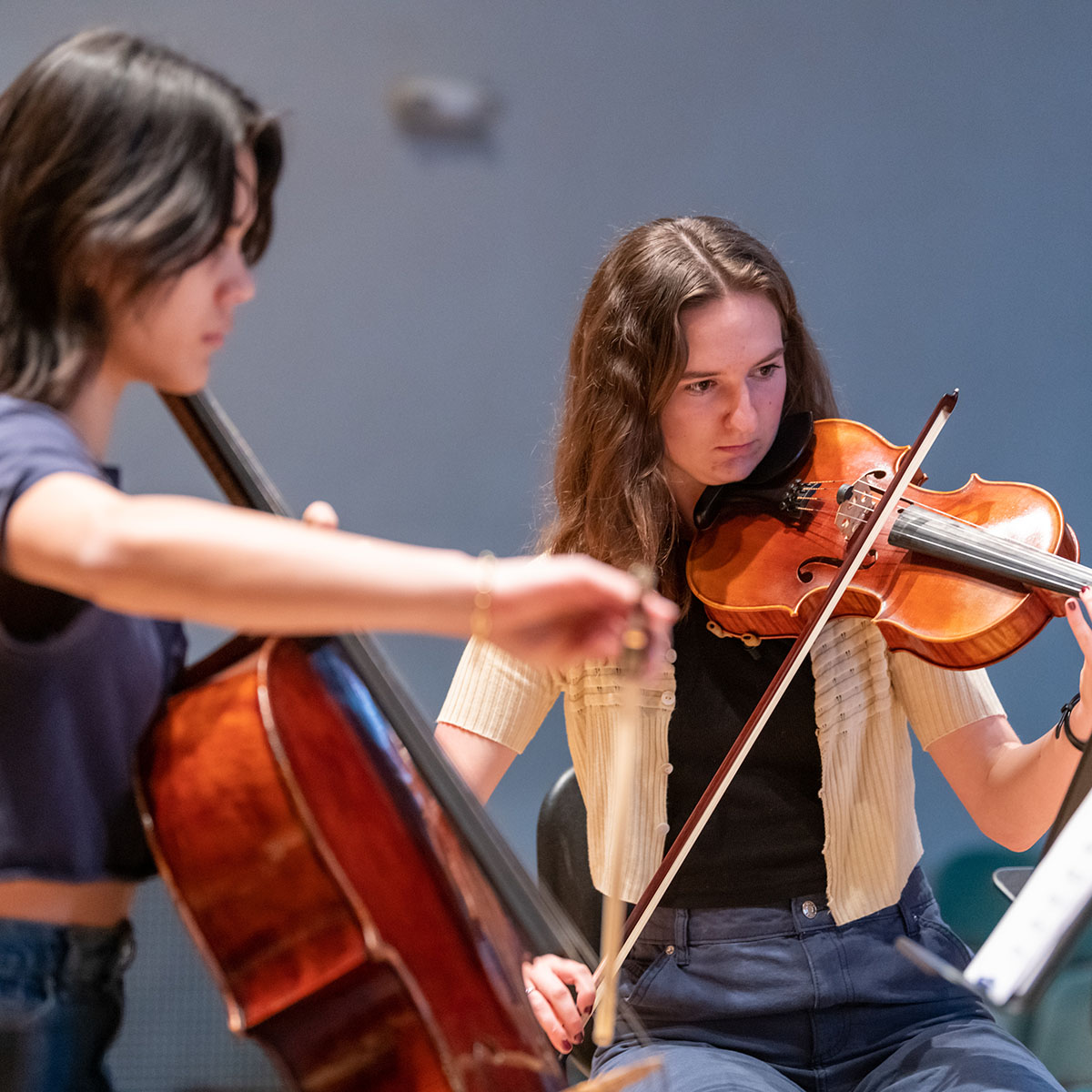 Two people sitting and playing music on a stage. One is playing the violin an the other is playing the bass.