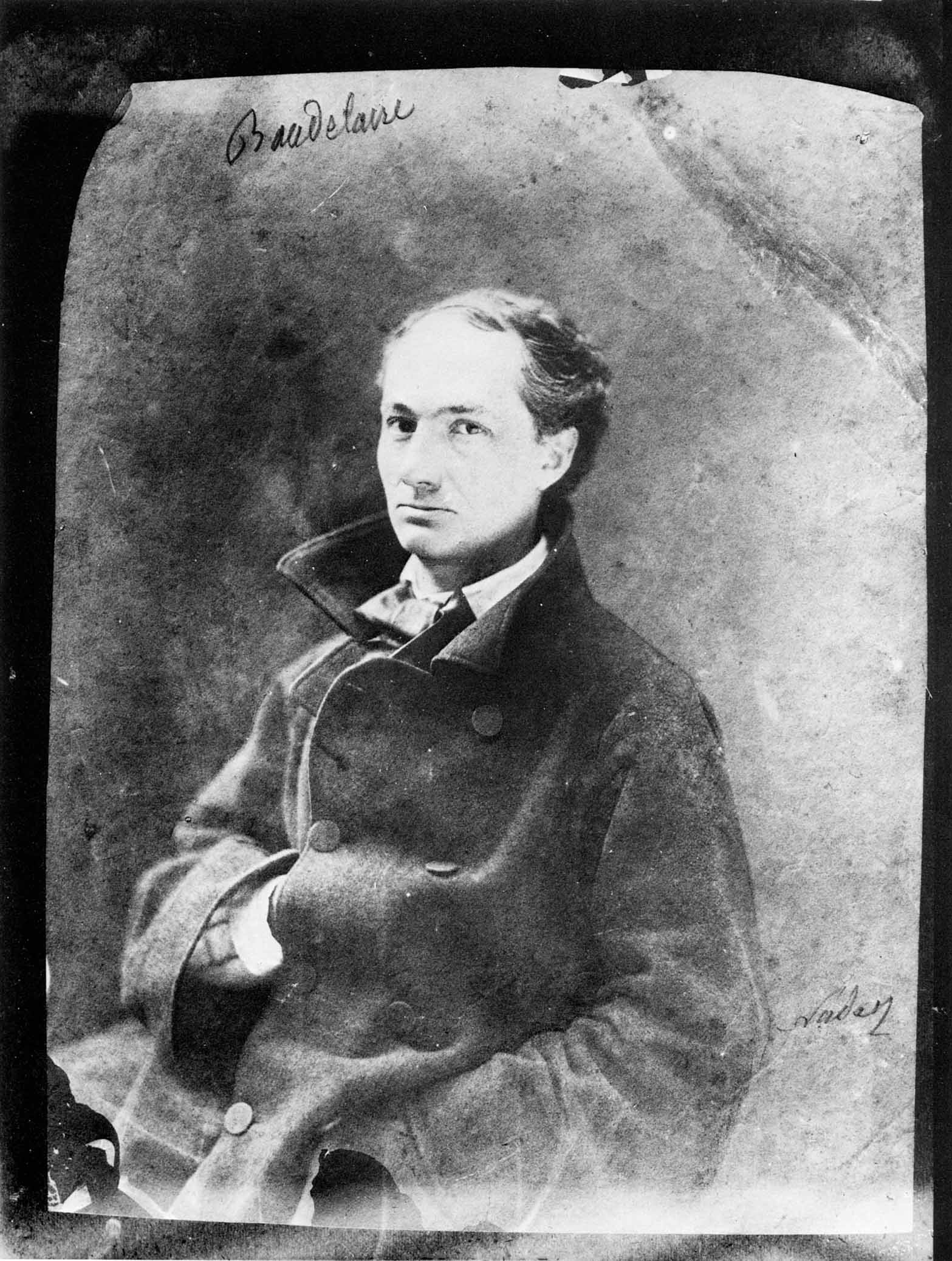 Black and white photo of Charles Baudelaire wearing a double buttoned, high collared coat. 