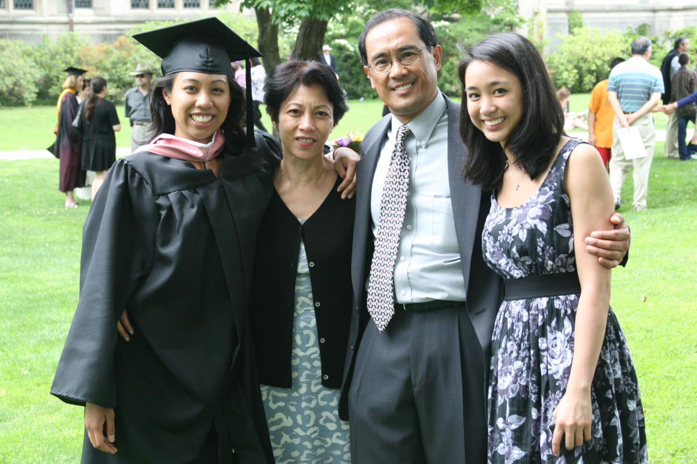 Four people smiling at the camera. One of the people is dressed in graduation robes.