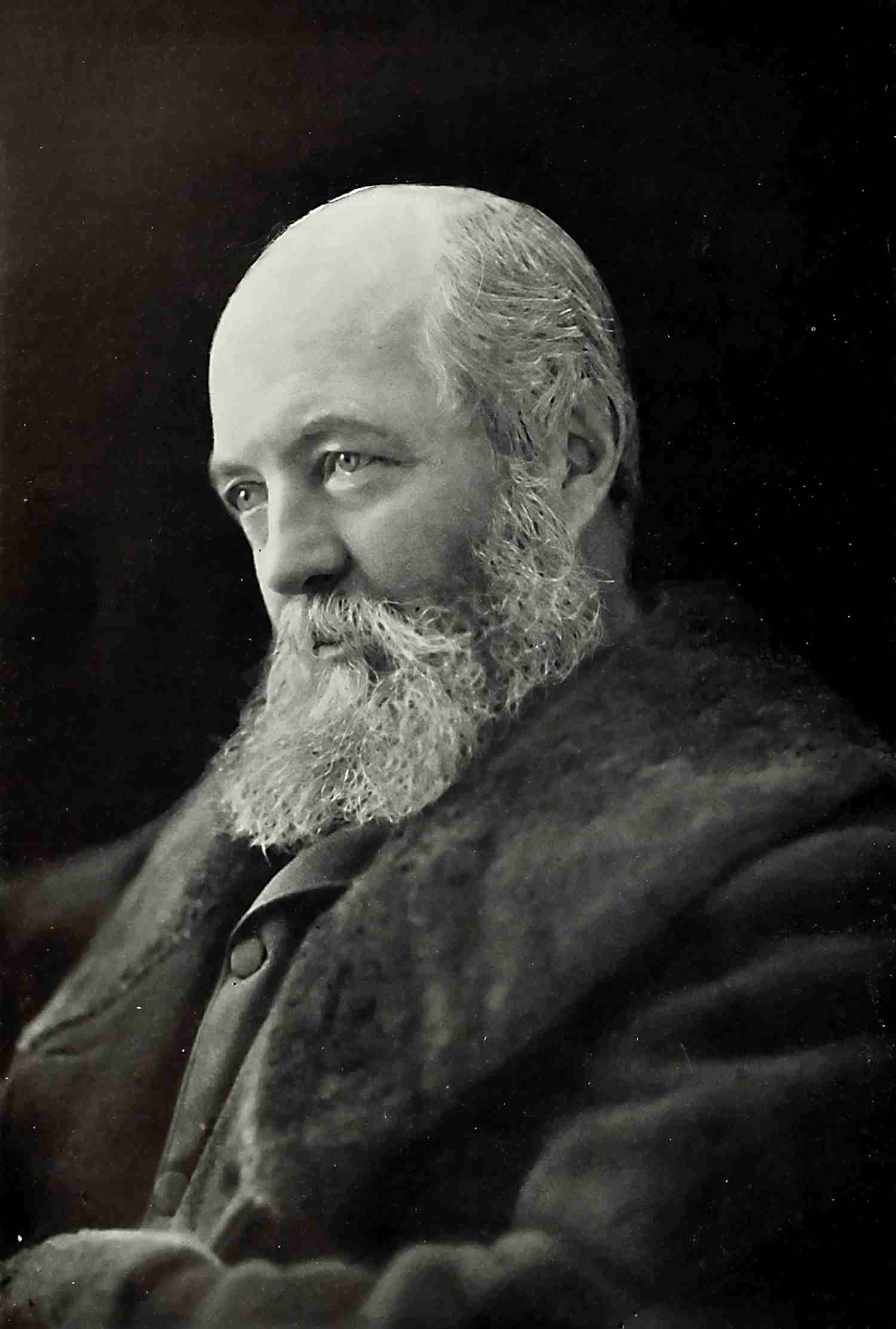 A historical portrait of Frederick Law Olmsted in 1893. Olmsted is a bald person with a long beard and a dark coat.