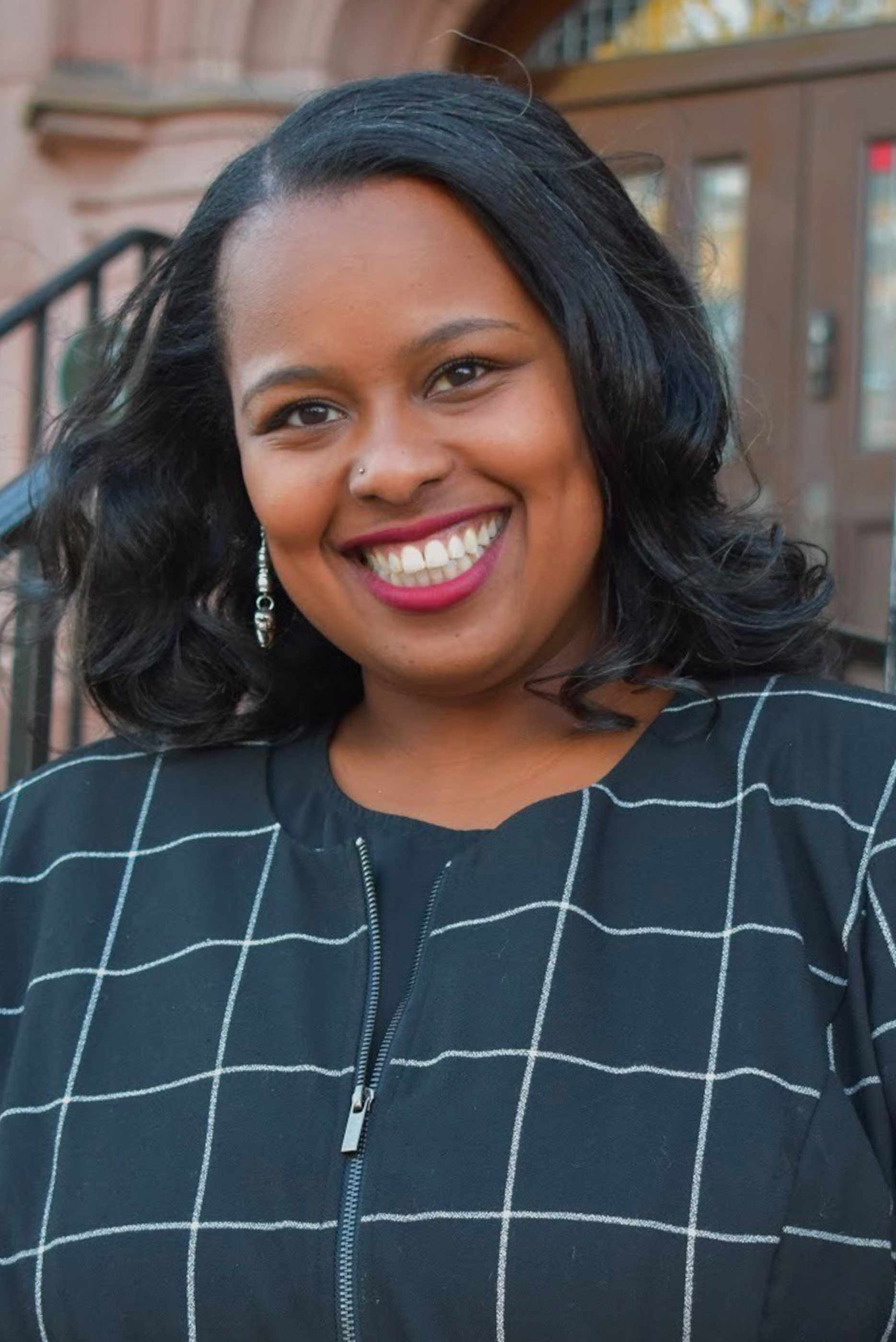 A portrait photo of Taneisha Means in front of a building on Vassar's campus.