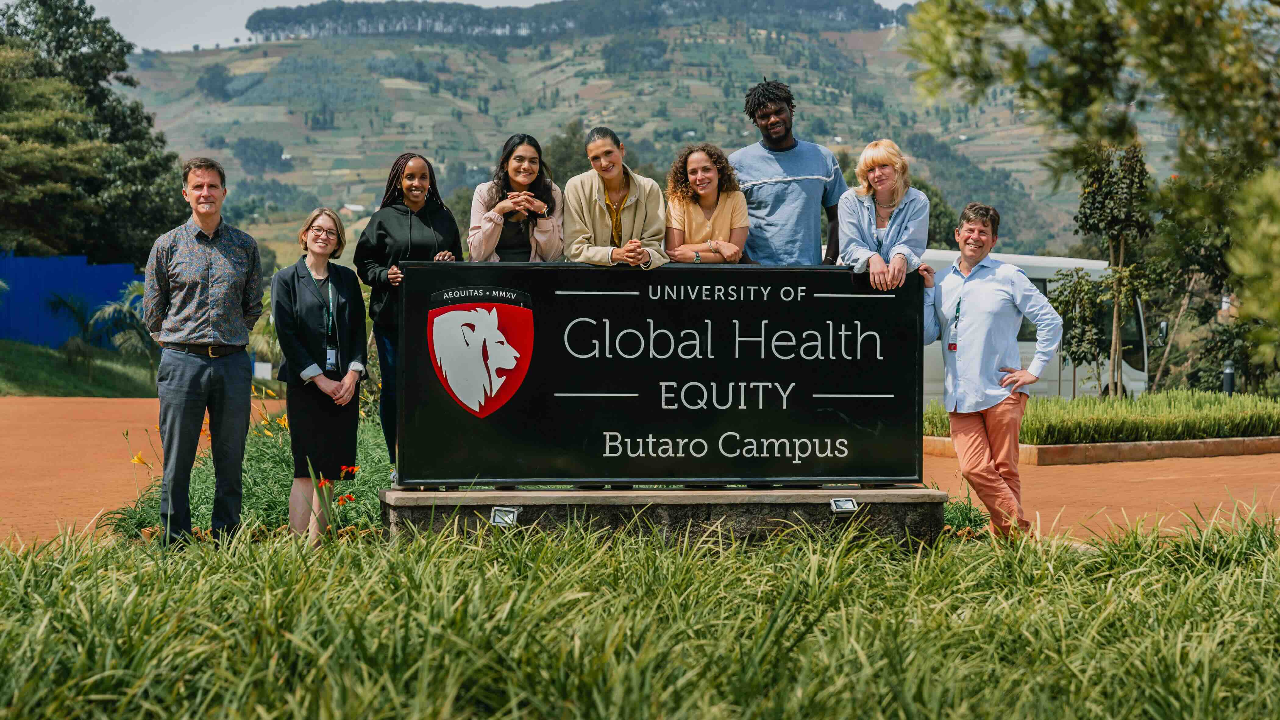 A group of people smiling and standing behind a sign that reads: The University of Global Health Equity, Butaro Campus.