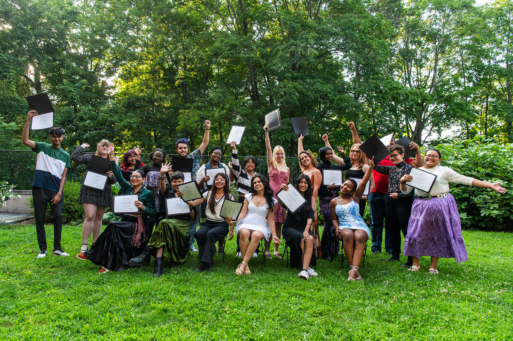 A large group of students who are standing in two lines holding up a diploma and smiling. 