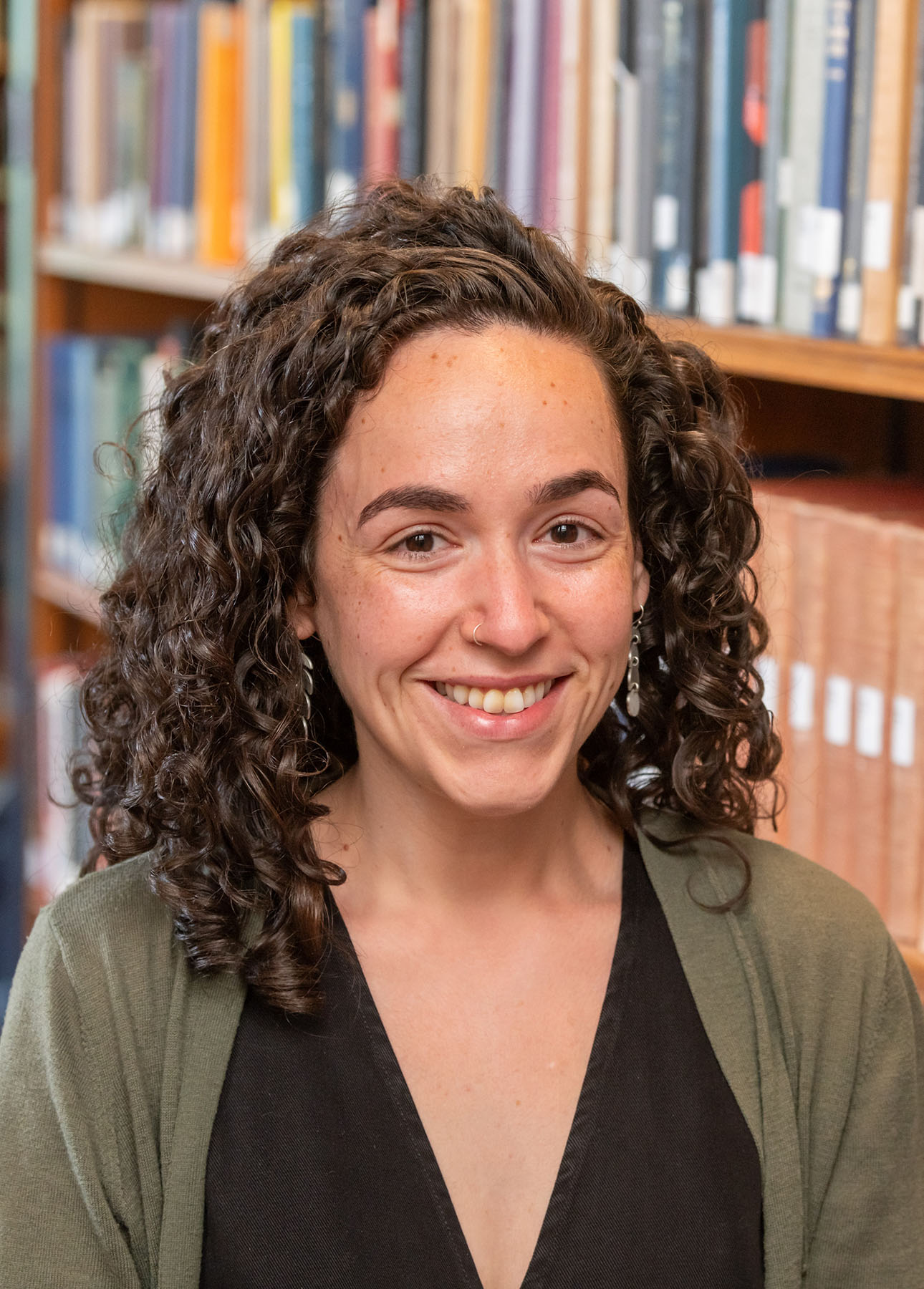 Person with long curly brown hair standing in front of a book case.