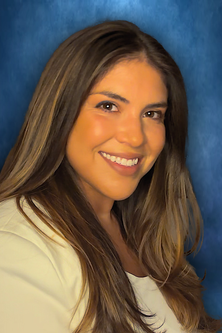 Portrait of a person with long brown hair and a white suit jacket smiling.