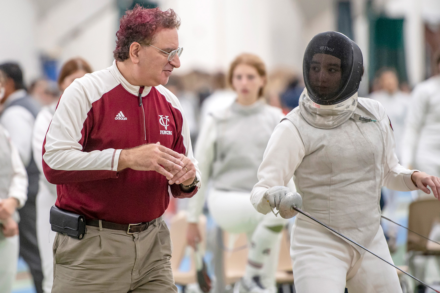 A person in full fencing gear standing next to a coach.