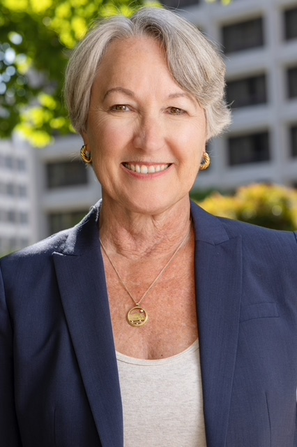 Person with neat blonde/grey hair with a suit jacket and white blouse smiling for a portrait.