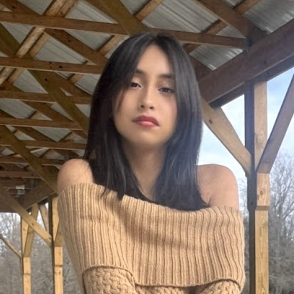 A headshot of Alexandra Tapia, a person with long black hair and a tan knitted sweater.