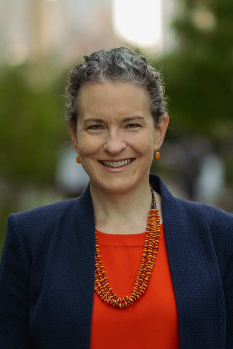 Anne Green ’93, a person with short gray hair, a dark coat, and a red shirt, smiles at the camera.