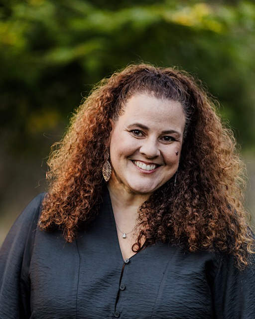 A portrait of Carolyn Kulic, a person with long brown curly hair and a gray shirt.