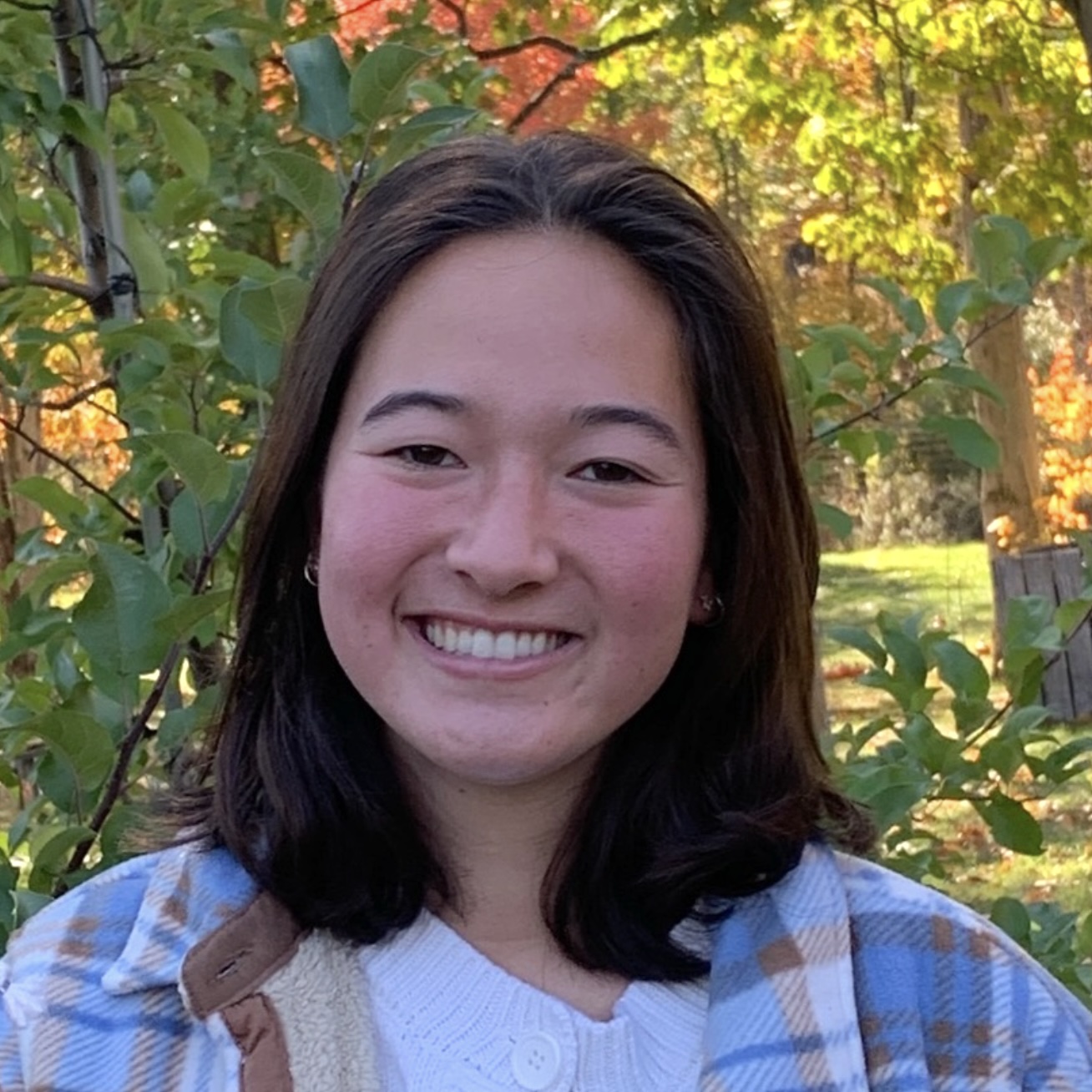 A headshot of Cassie Koyamatsu, a person with long dark hair and a plaid shirt.